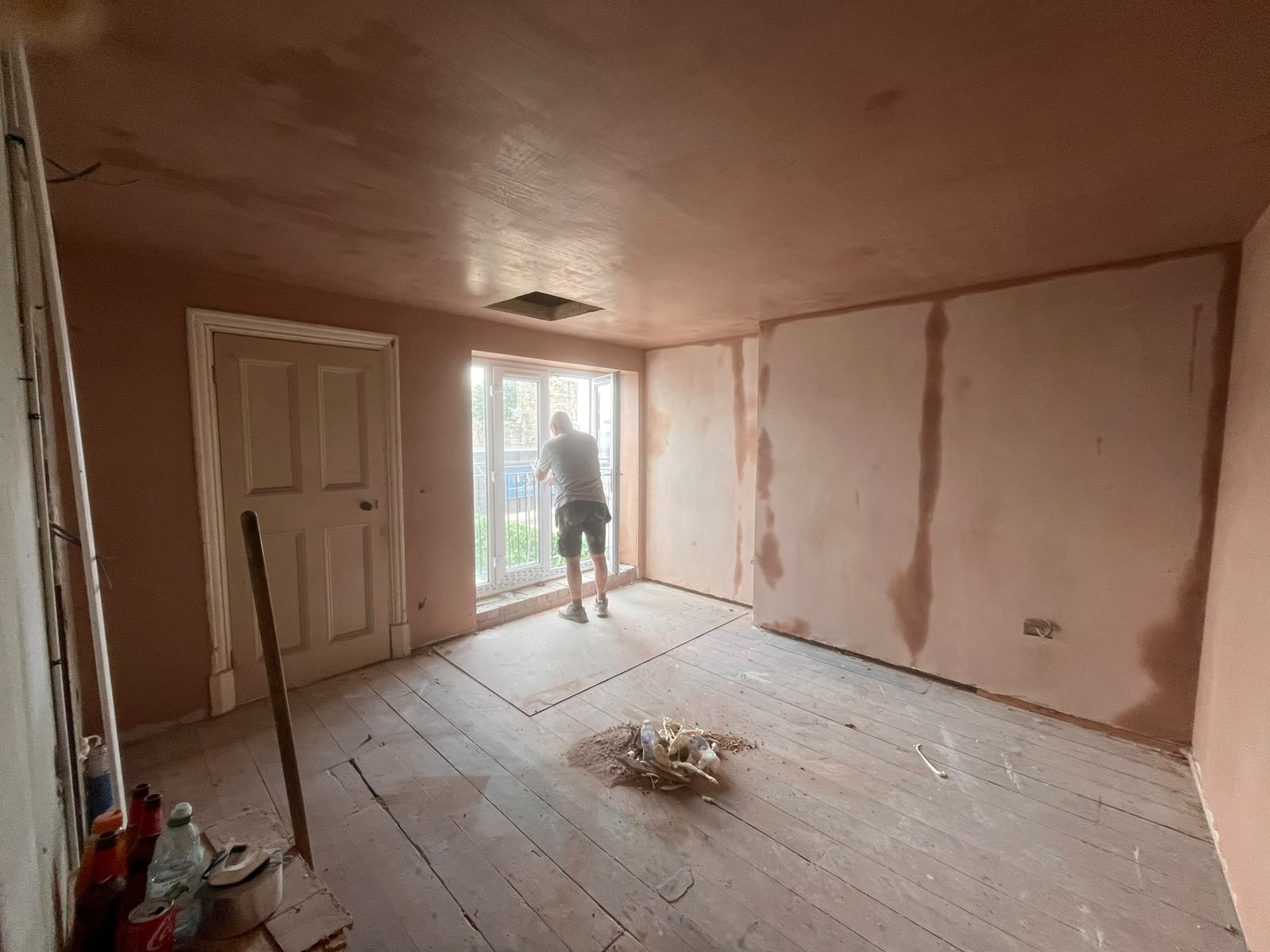Room with freshly skimmed plaster walls and ceiling, plasterer at the window, bare floorboards